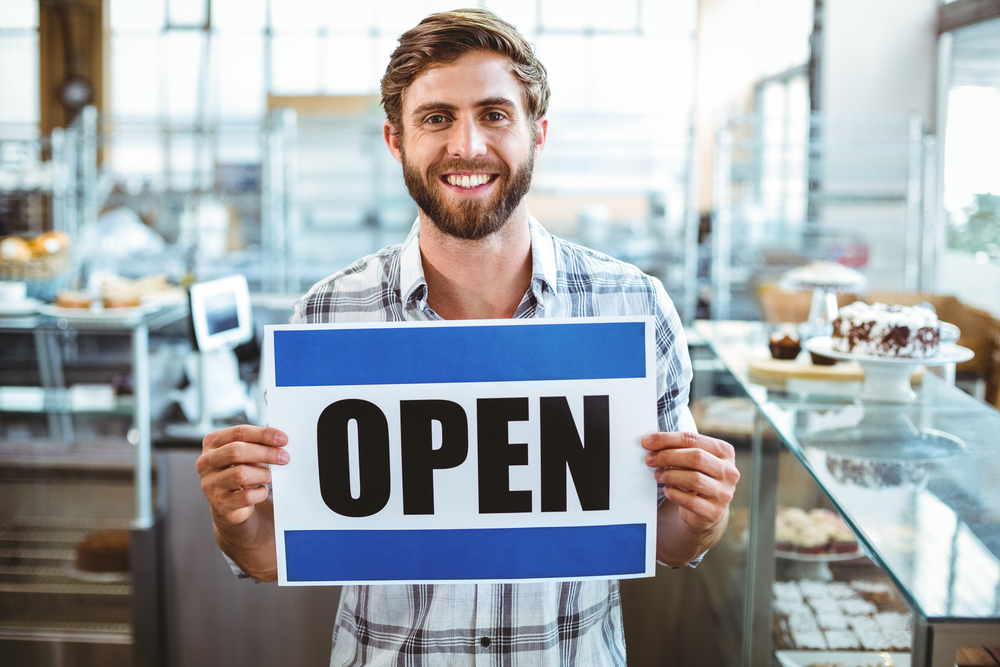 Owner holding an open sign with a smile on his face.