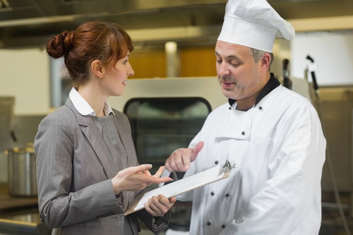 Jeune inspectrice discutant avec le chef cuisinier dans une cuisine professionnelle